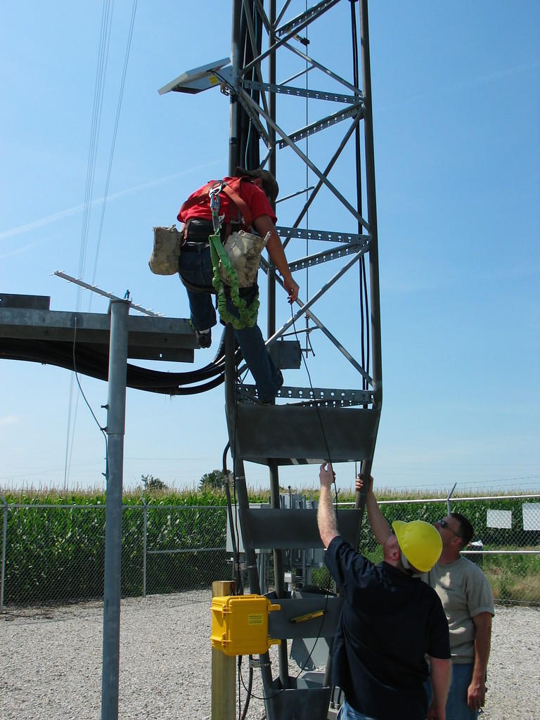 A Tower Tech employee has attached the 10 watt solar panel to the tower and is about to install the 900 MHz yagi antenna